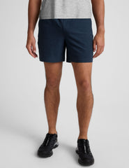 man wearing a grey t-shirt and navy blue shorts on a plain background.