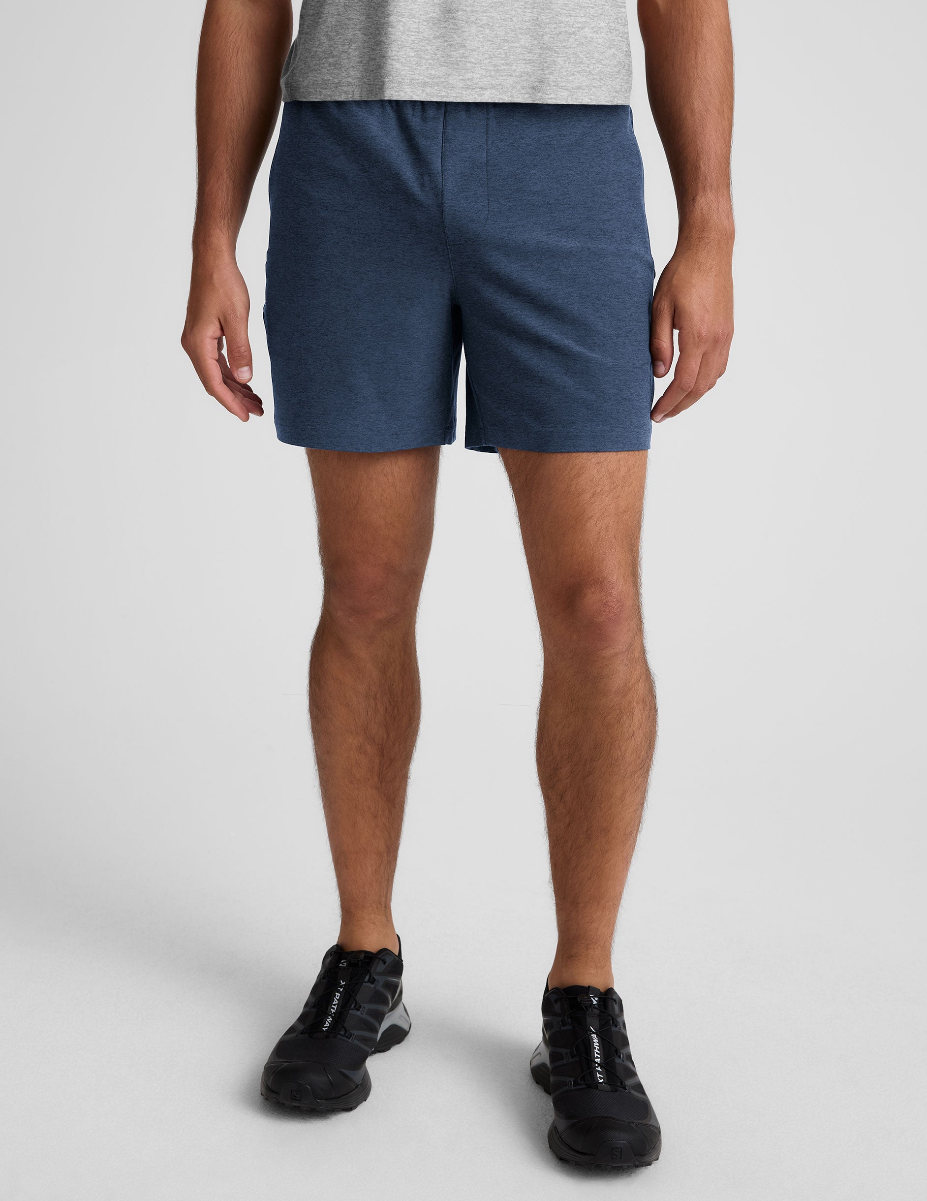 man wearing a grey t-shirt and blue shorts on a plain background.