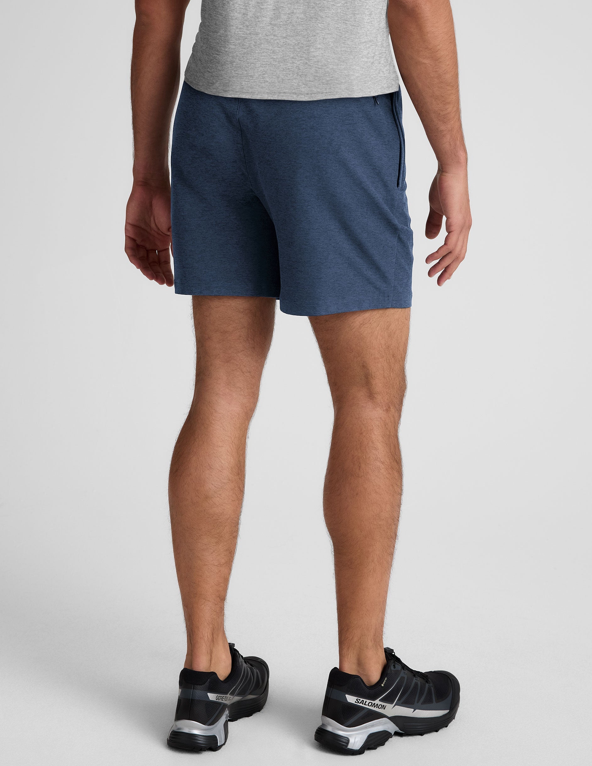 man wearing a grey t-shirt and blue shorts on a plain background.