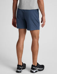 man wearing a grey t-shirt and blue shorts on a plain background.