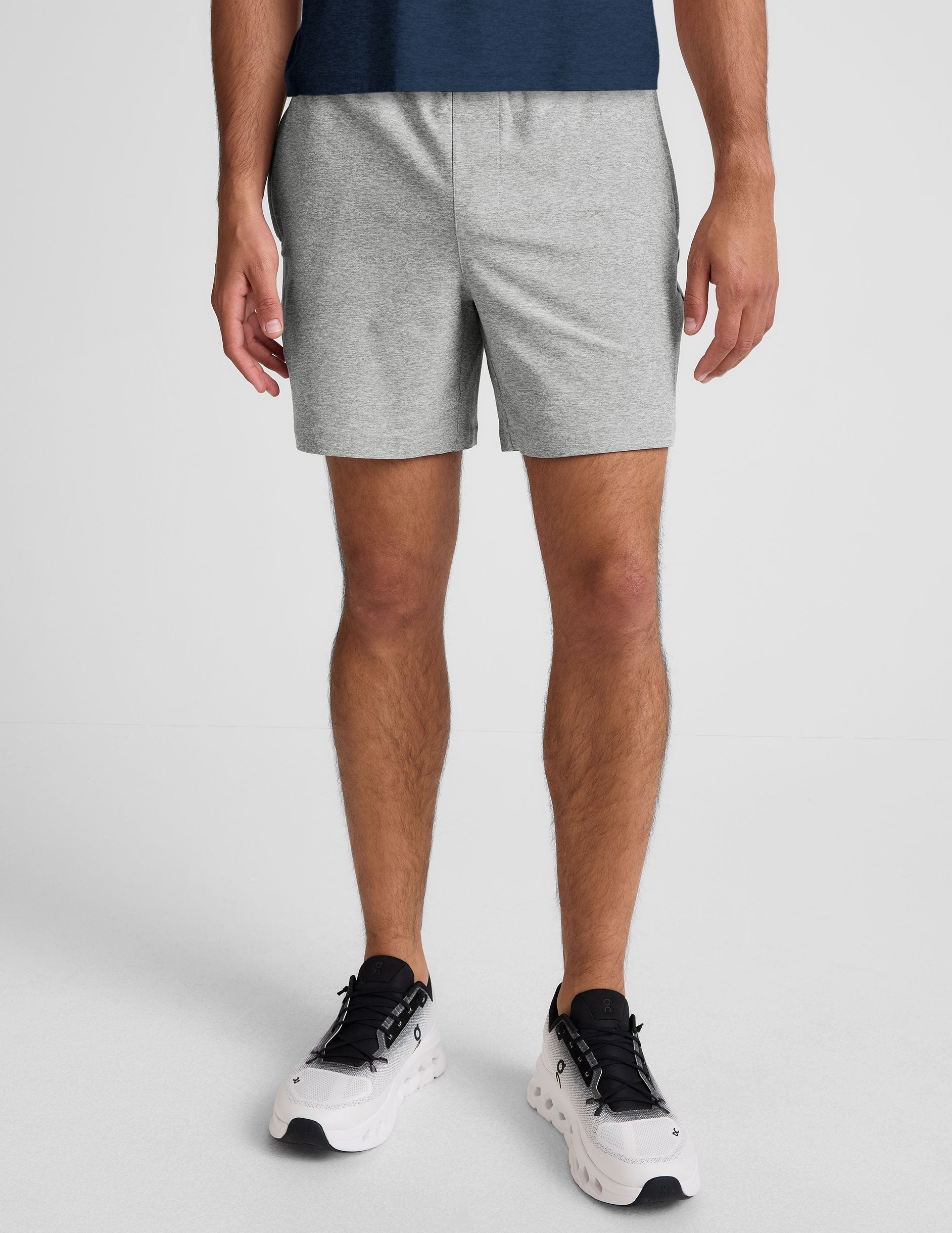 man wearing a navy t-shirt and gray shorts on a plain background.