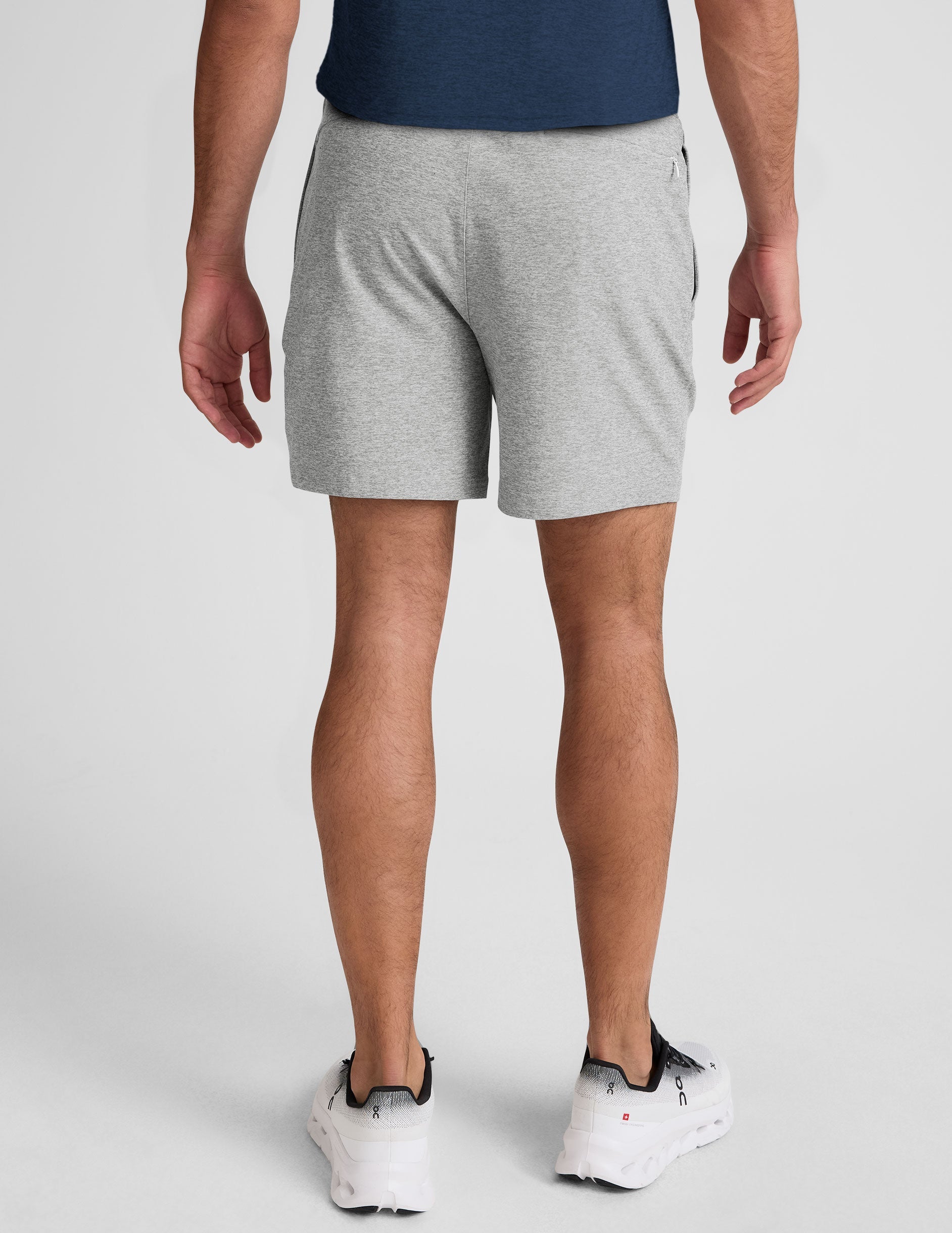 man wearing a navy t-shirt and gray shorts on a plain background.