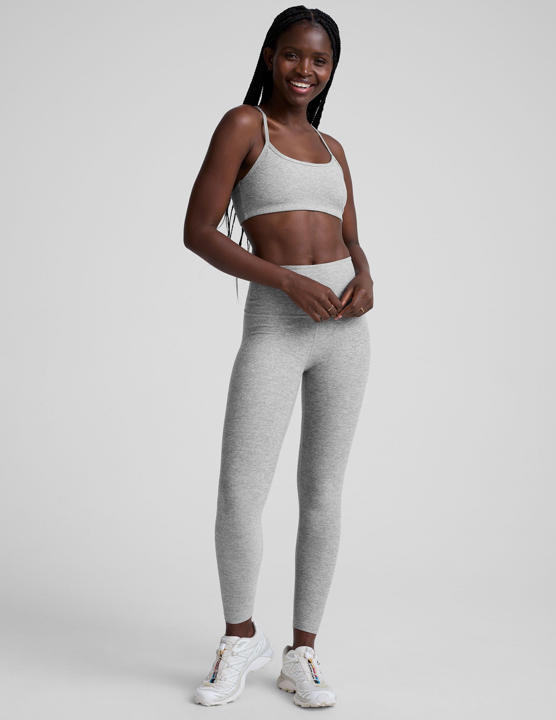 model is wearing a gray racerback bra with slim spaghetti straps and leggings against a plain background.