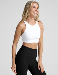 model wearing a white high-neck racerback sports bra and black leggings on a light gray background.