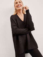 Woman wearing a brown sweater and black leggings against a plain background.