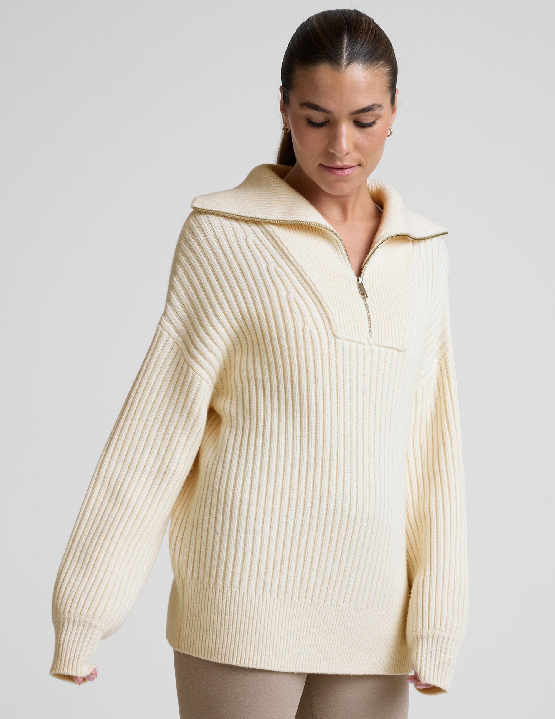woman wearing a white quarter zip collared sweater against a plain background.