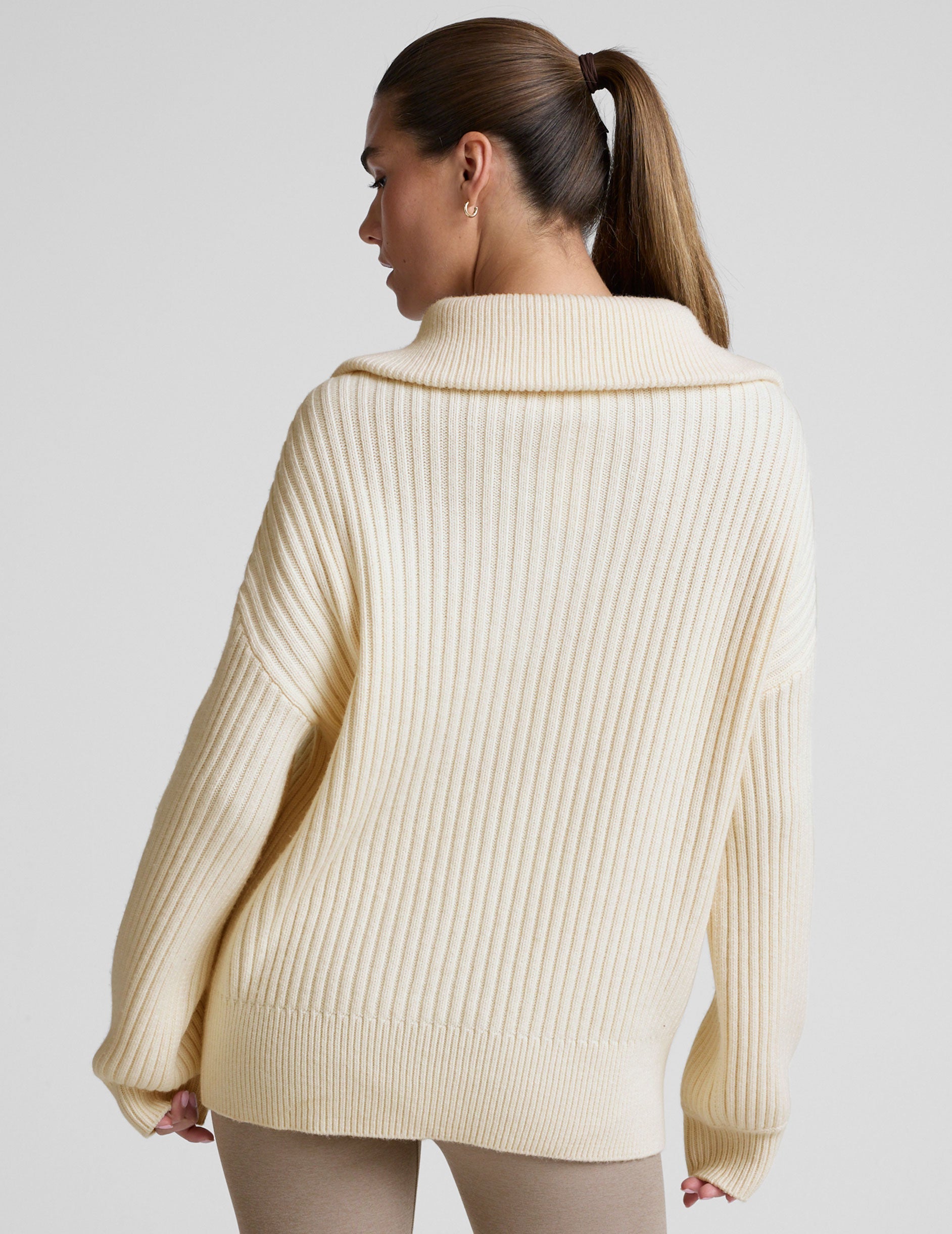 woman wearing a white quarter zip collared sweater against a plain background.