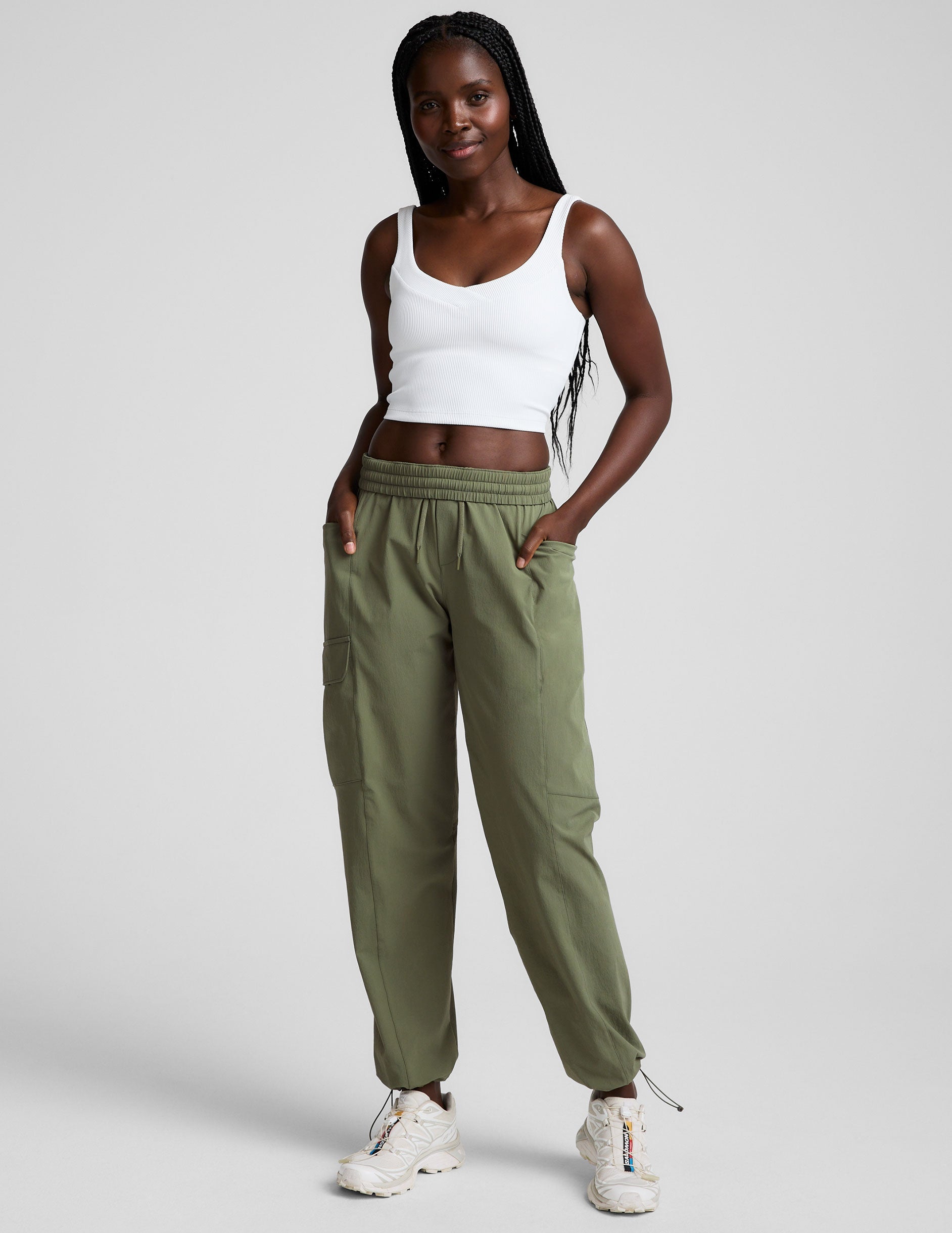 model wearing green pants and a white tank top on a plain background.