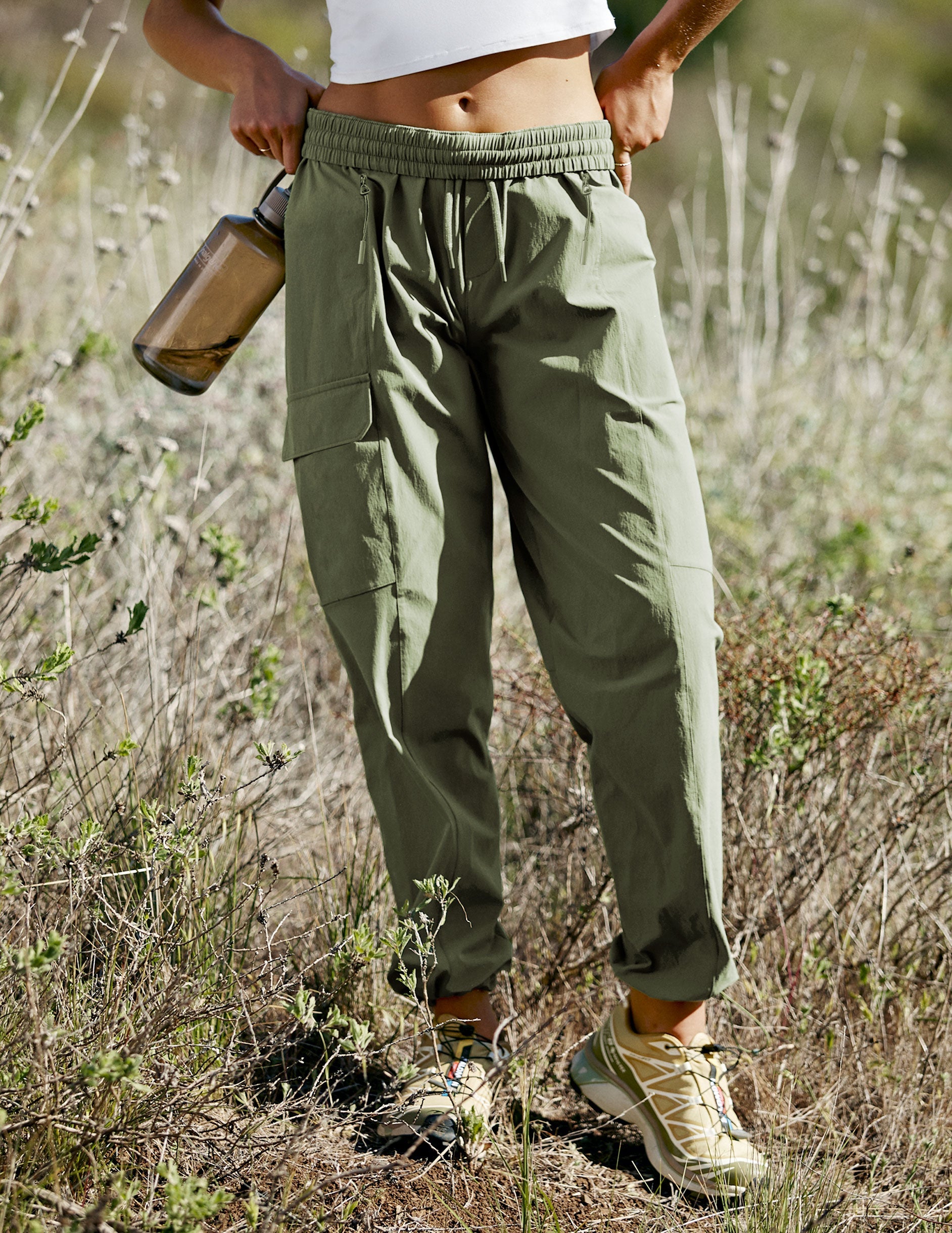 model wearing a white t-shirt and green cargo style pants walking on a trail in nature wearing a white top and green pants.