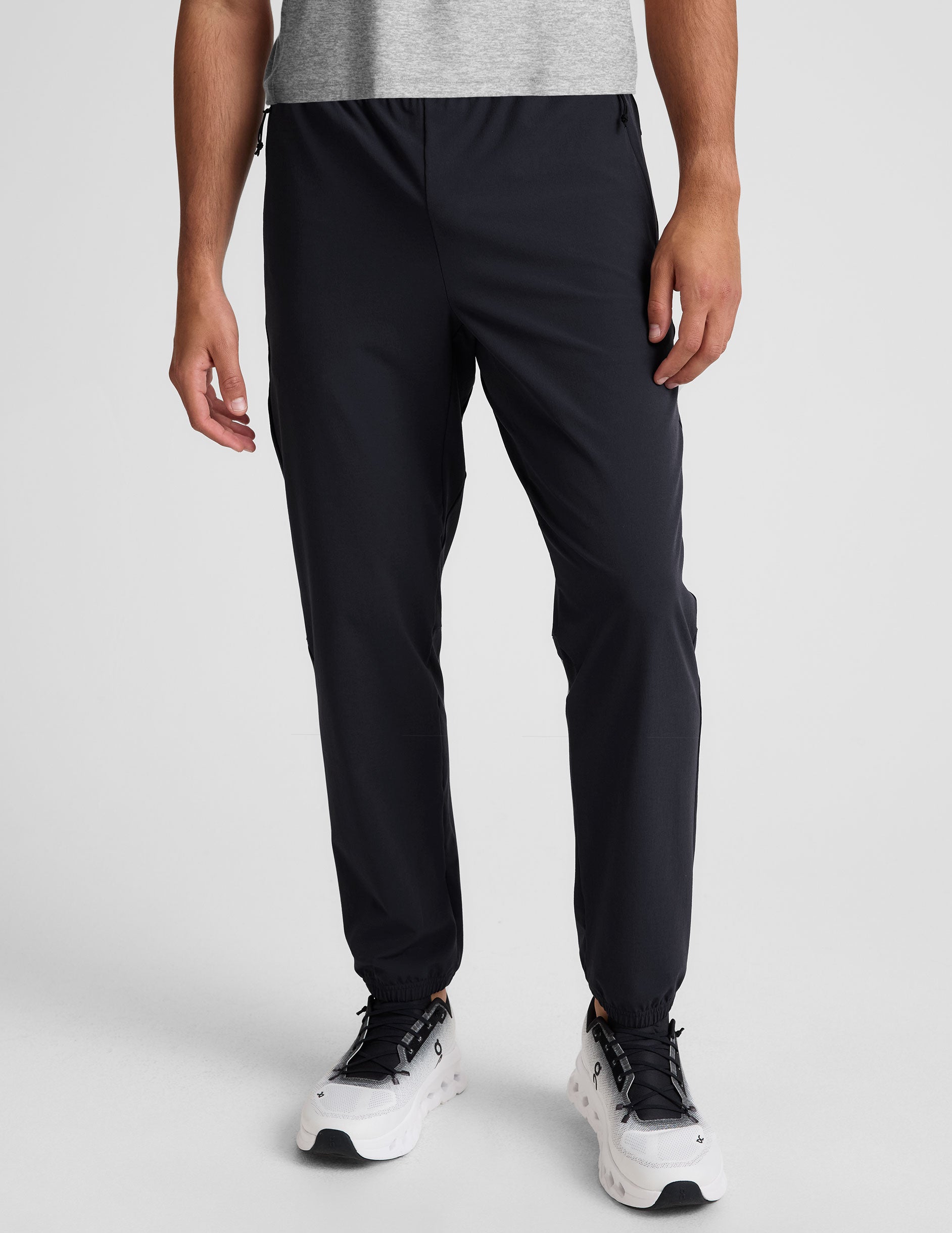 man wearing a gray crew neck t-shirt and blue joggers on a plain background.