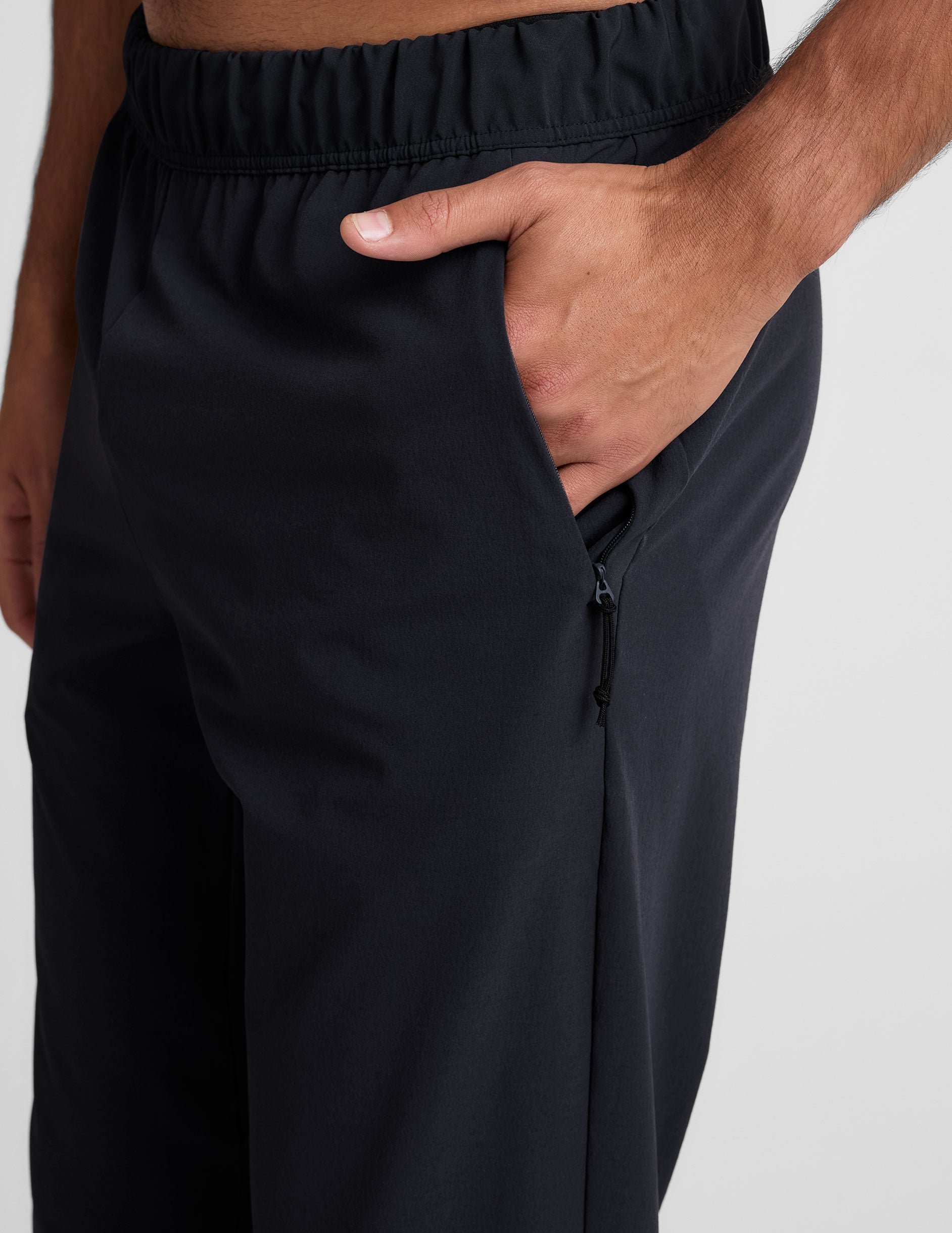 man wearing a gray crew neck t-shirt and blue joggers on a plain background.