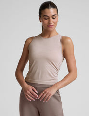 model is wearing a beige sleeveless top and brown pants against a plain background.