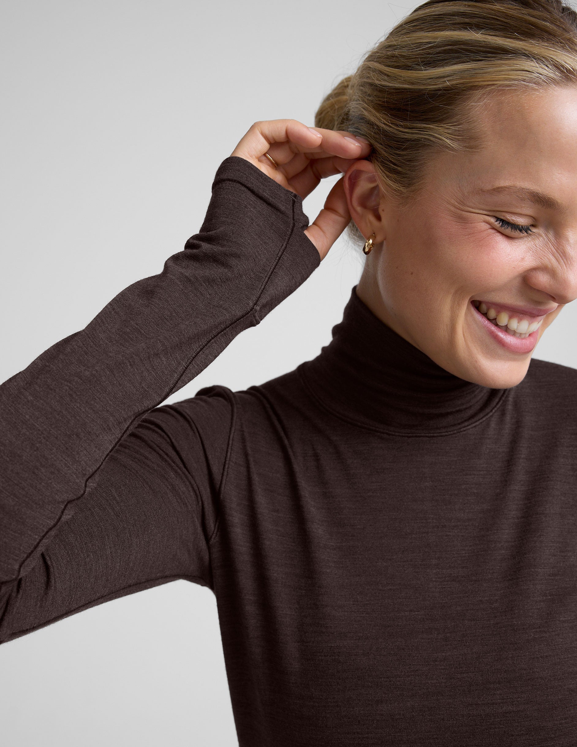woman wearing a brown turtleneck and pants on a light gray background.