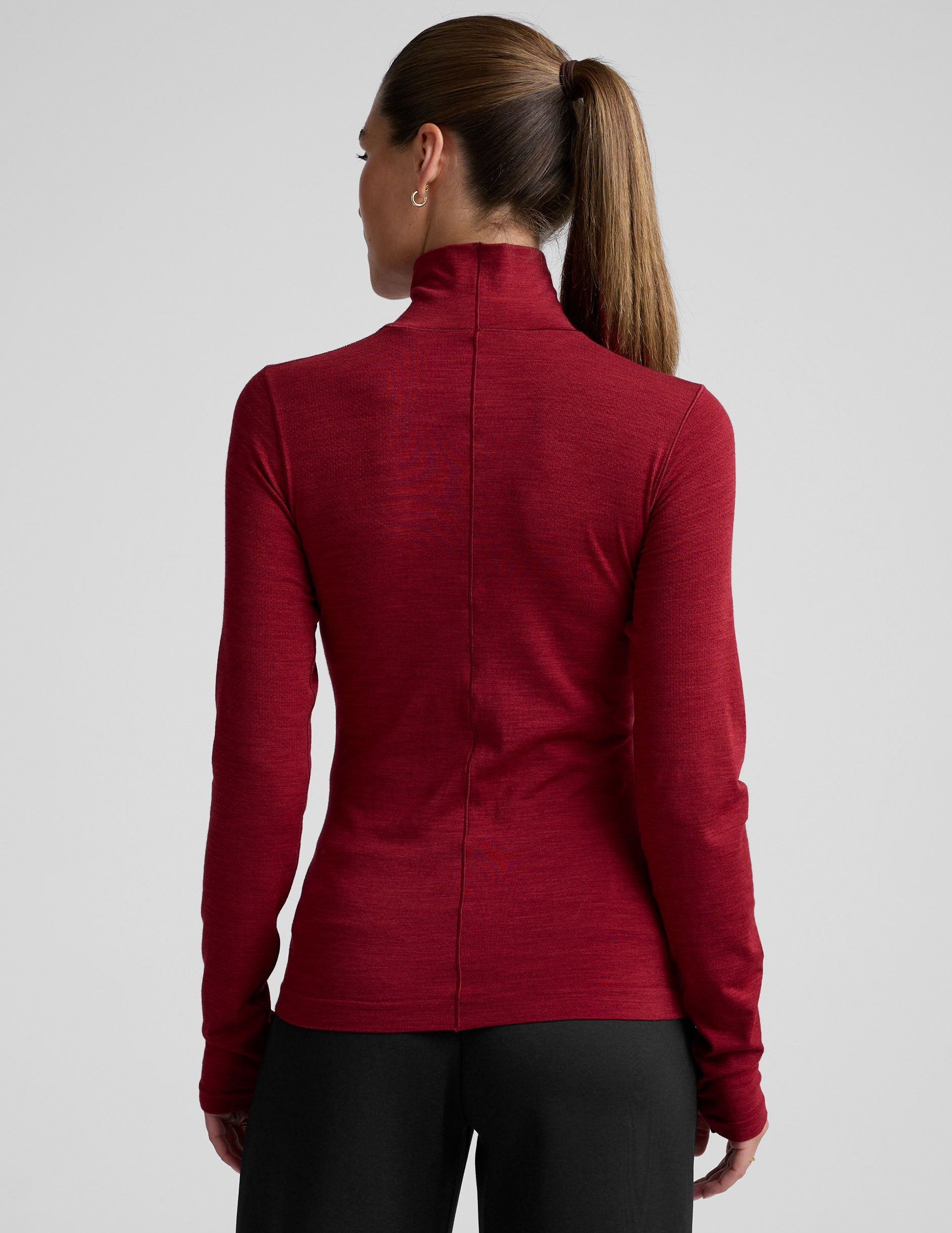 model wearing a red turtleneck long sleeve top and black pants on a plain background.